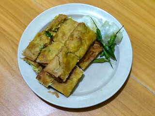 Egg martabak. Egg martabak is a traditional Indonesian food that tastes savory and delicious, served on a plate with pickles and chili.