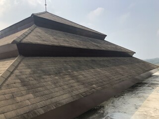 Weathered roof with asphalt shingles, partially lifted and deteriorated, captured from a low-angle...