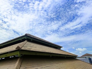 View of a worn asphalt shingle roof under a bright blue sky, showing visible damage and signs of aging on the roofing structure