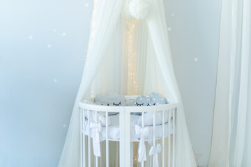 Crib in a modern nursery room. Baby cot with canopy. Stylish scandinavian interior design of newborn baby room with bed and pillows. Hanging white canopy with cradle. Decor child room with furniture.  © stock_studio