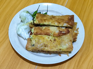 Egg martabak. Egg martabak is a traditional Indonesian food that tastes savory and delicious, served on a plate with pickles and chili.