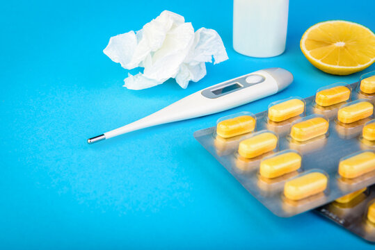 Various medicines, lemon, thermometer, sprays from stuffy nose and pain in throat on blue background. Treatment of colds and flu.