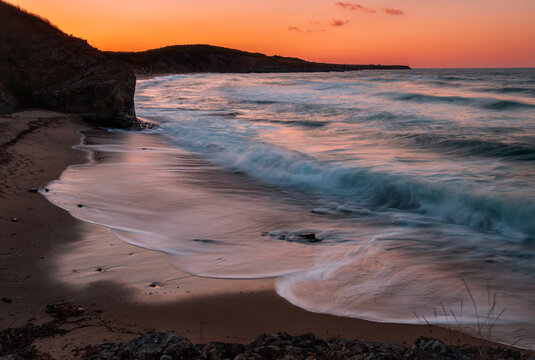 Long exposure creating soft waves gently lapping the shoreline during a vibrant sunset. European landscape. 
