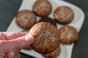 Hand is holding a chocolate coated ginger bread before eating it,. More ginger bread blurry on a white plate in the background. Close up.