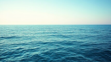 Obraz premium Calm ocean scene at sunrise, featuring a vast expanse of tranquil blue water under a pale sky. Subtle wave textures are visible on the water's
