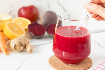 Red beet juice made with ginger, apple, carrot, and lemon in a glass with hand holding a straw....