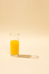 Glass of vibrant orange juice against a warm-toned background. The soft natural shadows add depth and elegance to the scene, creating a refreshing and modern aesthetic. Perfect for food and beverage