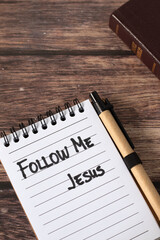 Follow Me, Jesus, handwritten quote in notebook with holy bible book on wooden background. Top view. Christian obedience, guidance, and faith, biblical concept.