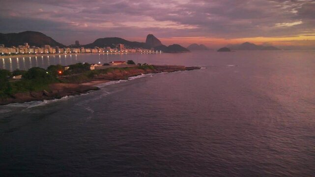 Sunrise in Arpoador Beach in Rio de Janeiro with orange sky and mountains at distance