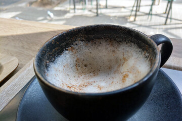 Cozy Cafe Ambiance: Foamy Cappuccino in Rustic Black Mug for Relaxation and Reflection