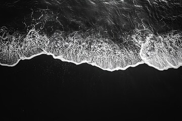 Aerial View of Ocean Waves Crashing onto a Dark Sandy Beach Creating a Stark Contrast