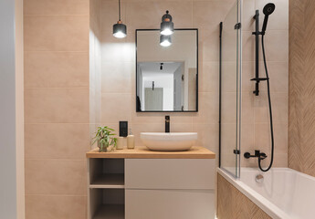 Modern interior of bathroom with ceramic wash basin with black faucet , bath with glass, tile on the wall and mirror. Luxurious hygiene room in industrial style with shower and bathroom sink.