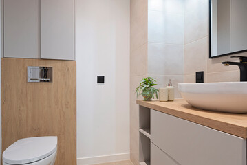 Modern interior of bathroom with white ceramic wash basin on the counter with black faucet , toilet, white tile on the wall. Luxurious hygiene room in industrial style. Real estate.