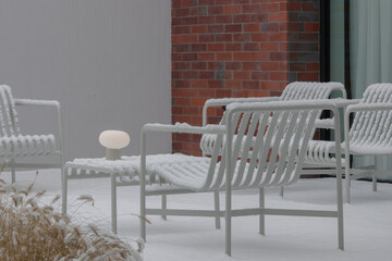 Patio Lounge Chairs and Table covered in snow. Portable lamp as design element.