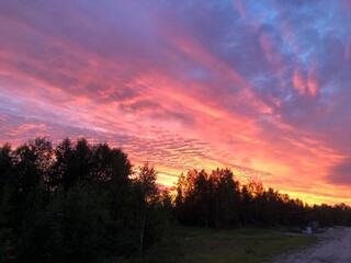Stunning sunset paints sky with vibrant hues of red, orange, and pink, blending into deep blues and purples. Silhouetted hills create contrast against fiery horizon, adding drama to serene landscape.