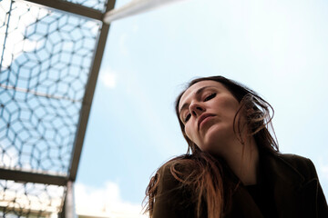 Young woman posing under modern architecture looking down at camera