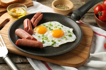 Tasty fried eggs with cut sausages served on wooden table, closeup