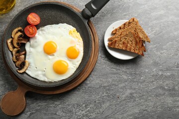 Tasty fried eggs with mushrooms served on grey table, flat lay