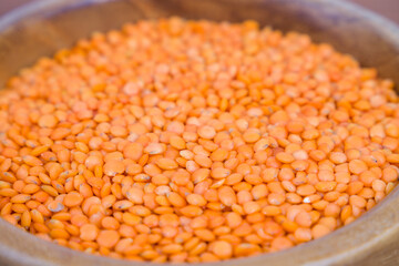 Red lentils in wooden bowl, closeup of legumes.