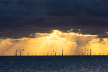 Dark clouds of a thunderstorm over silhouettes of wind turbines in the North sea in the backlit of the evening sun