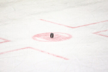 Black rubber puck standing vertical on a ice hockey rink face off circle middle.