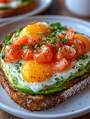 Toast with avocado fried eggs and tomato topping on a white plate on a wooden table