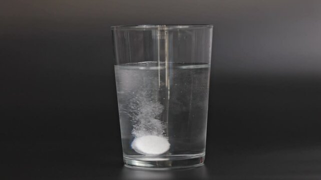 Effervescent tablet dissolves with bubbles in pure water isolated black background
