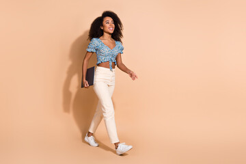 Full length photo of adorable lovely girl wear blue top holding modern device walking empty space isolated beige color background