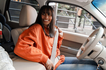 Young woman fastening seat belt smiling and looking back inside car