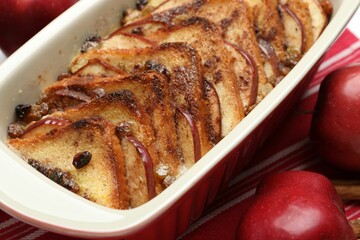 Delicious bread pudding in baking dish and fresh apples on table, closeup