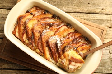 Taking tasty bread pudding from baking dish at wooden table, top view