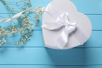 Beautiful wedding gift, ribbon and gypsophila flowers on light blue wooden table, flat lay
