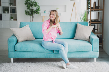 Obraz premium Young woman enjoying leisure time at home while brushing hair on a stylish sofa in natural daylight
