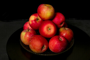 A pile of apples on a glass plate. Black background.