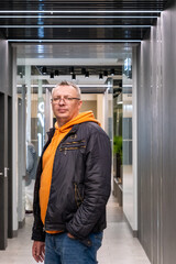 Portrait of a cheerful middle-aged man wearing a gray hoodie, standing against a textured stone...