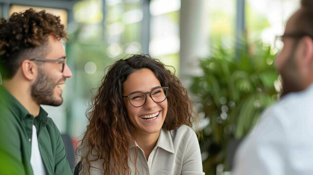 Happy and engaged colleagues having a friendly discussion in a modern, sustainable office with natural light and green plants.