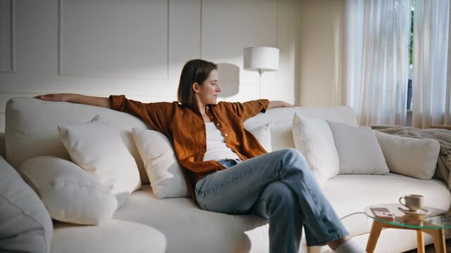 Carefree lady falling couch with soft pillows. Smiling woman sit down home sofa