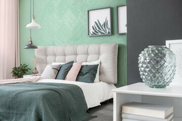Elegant bedroom interior design with colored marble wall, wooden flooring, king sized comfy bed, hanging lamps above, white wooden furniture, painting frames on wall, colored curtains. 3D Rendering