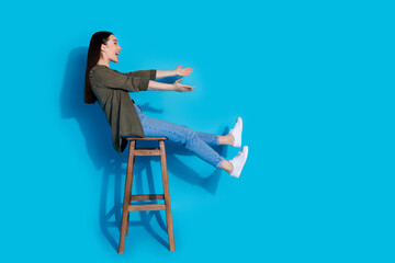 Young woman on a stool with arms extended in enjoyment against a vibrant blue background