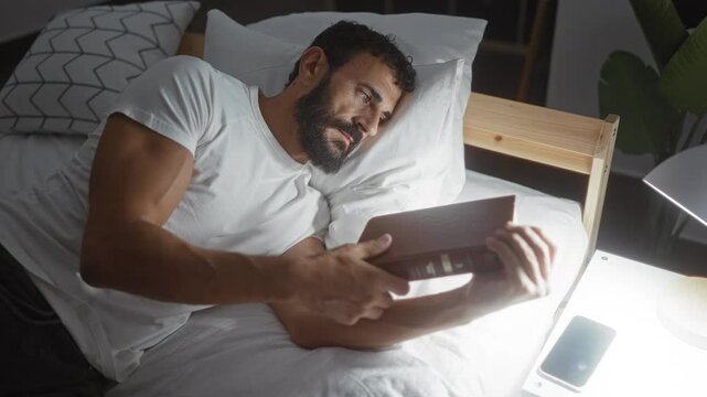 Young man with a beard in a bedroom lying on bed reading a book and preparing to sleep, depicting relaxation and home comfort in a cozy indoor setting. - Powered by Adobe