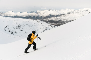 One-armed confident skier skis up the slope against a background of a beautiful mountains