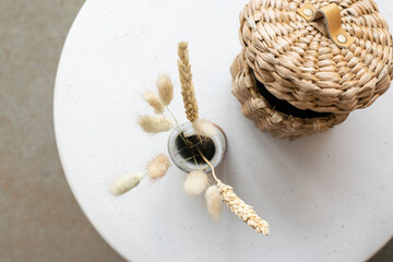 Top-down view of a ceramic vase with dried flowers and a wicker basket on a white round table