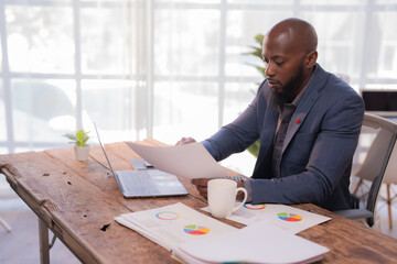 Businessman reviewing paperwork and analyzing financial data with charts and graphs, working diligently at his desk in a modern office environment