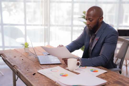 Businessman reviewing paperwork and analyzing financial data with charts and graphs, working diligently at his desk in a modern office environment