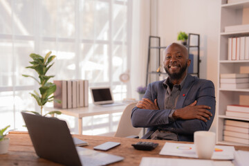 Fototapeta premium Confident African American entrepreneur sitting with crossed arms at his desk in a modern office, smiling towards the camera, exuding professionalism and success in his business venture