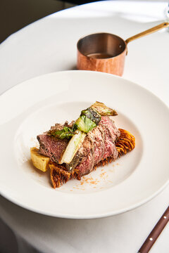 A beautifully presented gourmet dish of tender meat accompanied by roasted vegetables and sauce, served on a fine white plate in a sophisticated dining atmosphere
