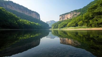 Obraz premium A serene river reflects lush green cliffs under a clear blue sky, showcasing the beauty of nature and tranquility.