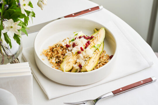 A delicious dish with fresh zucchini filled with quinoa and garnished with pomegranate sits on a white table setting alongside a floral centerpiece