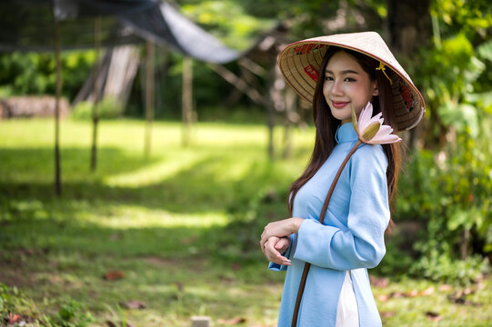 Portrait of Vietnamese woman in traditional Ao Dai dress holding lotus flower in the park