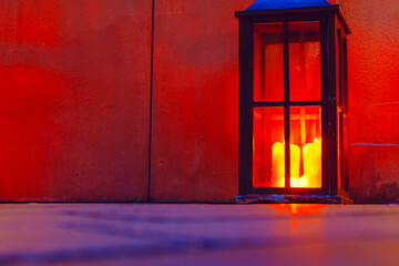 Lantern with glowing candles casts warm light against a textured wall. The flickering flames create...